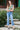 Woman in cropped denim jeans, paired with a tropical print top and heels, standing on steps outside.